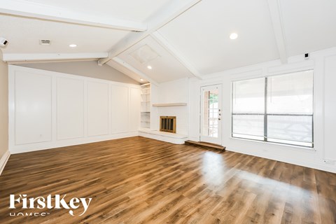 A spacious room with wooden floors and white walls, with a large window on the right side.