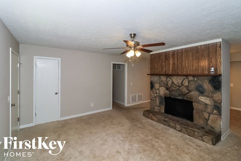 A living room with a stone fireplace and a ceiling fan.
