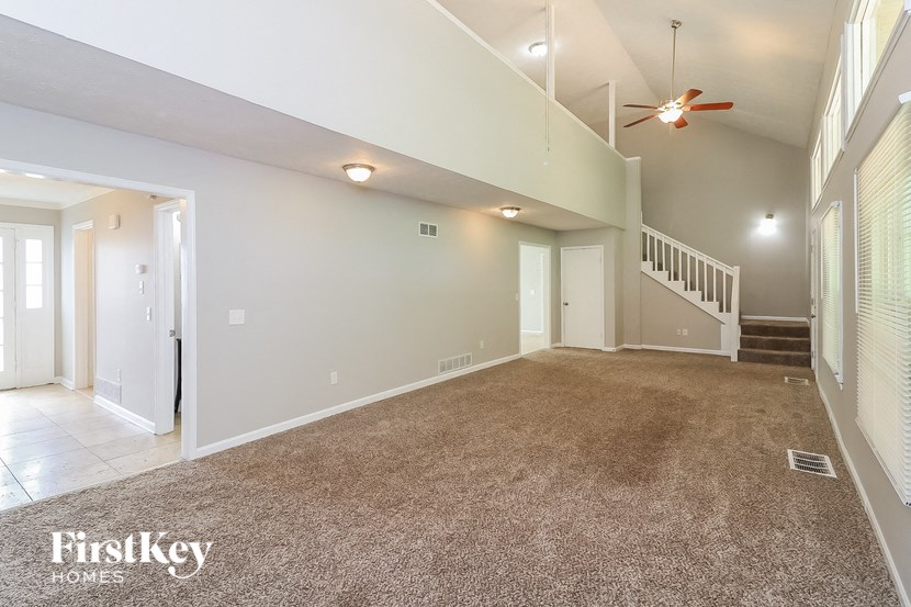 A spacious living room with a carpeted floor and a staircase leading to another room.