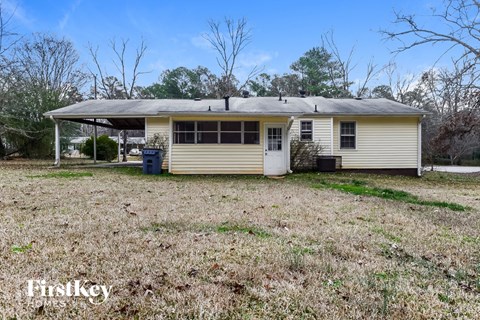 A small house with a porch and a covered area is surrounded by a grassy field.