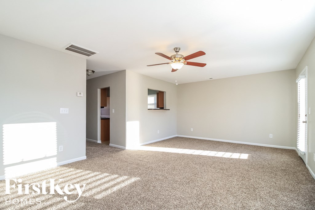 A spacious room with a carpeted floor and a ceiling fan.