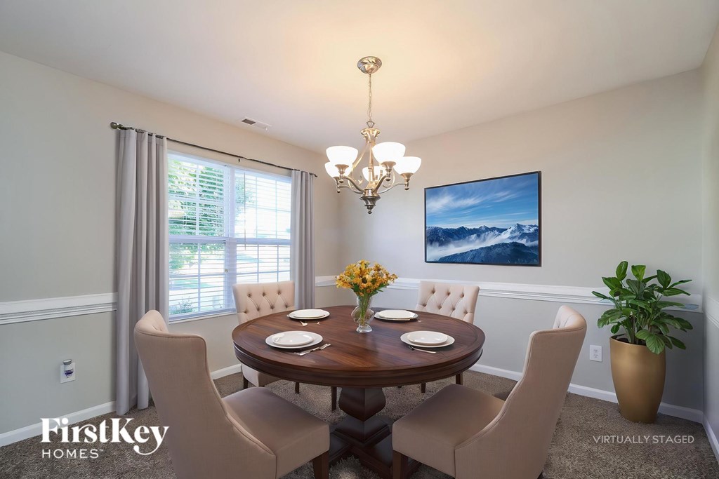 A dining room with a wooden table and chairs, a chandelier, and a painting on the wall.