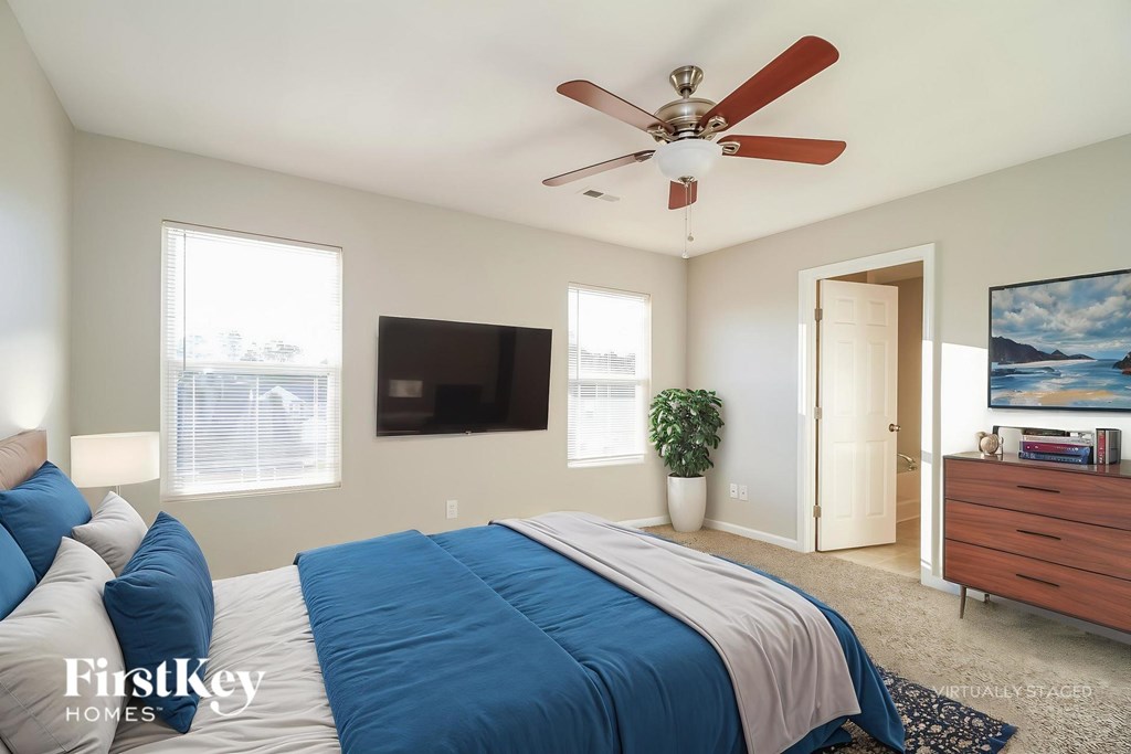 A bedroom with a bed, a ceiling fan, and a painting on the wall.