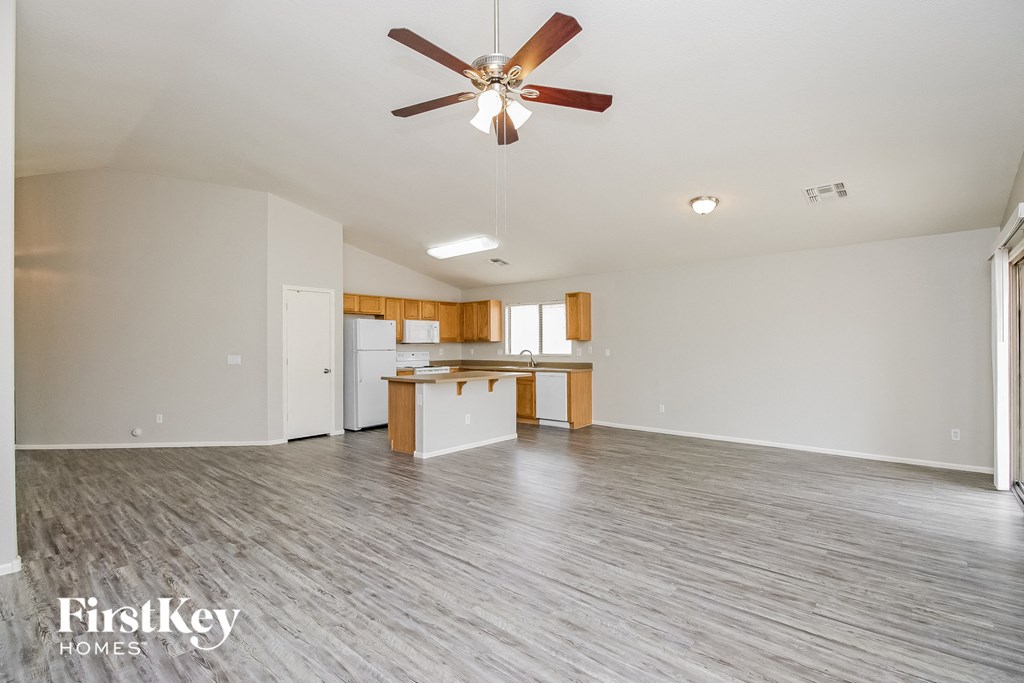 an empty living room with a ceiling fan and a kitchen