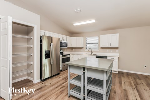A kitchen with a refrigerator, oven, and a table with shelves.