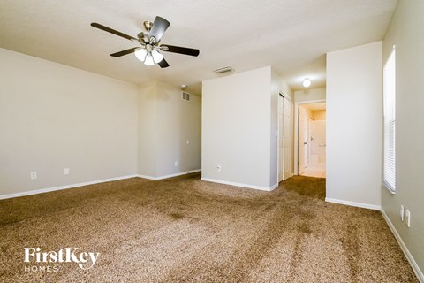 a spacious living room with carpet and a ceiling fan