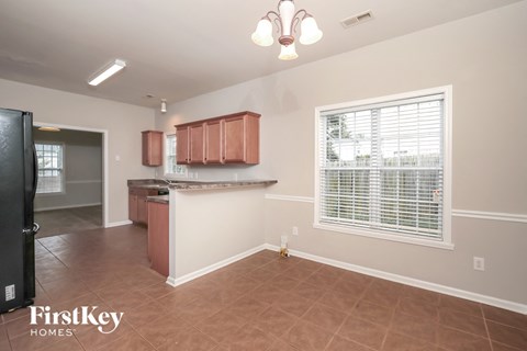A kitchen area with a refrigerator, cabinets, and a window with blinds.