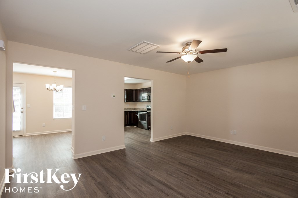 an empty living room with a ceiling fan and a kitchen