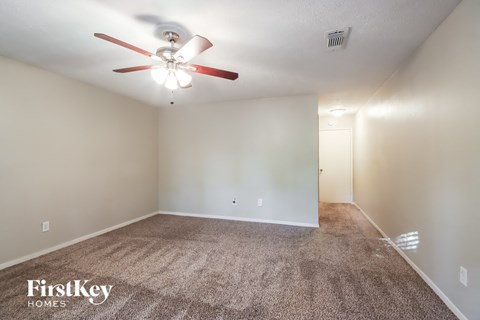 the living room is spacious with carpet and a ceiling fan