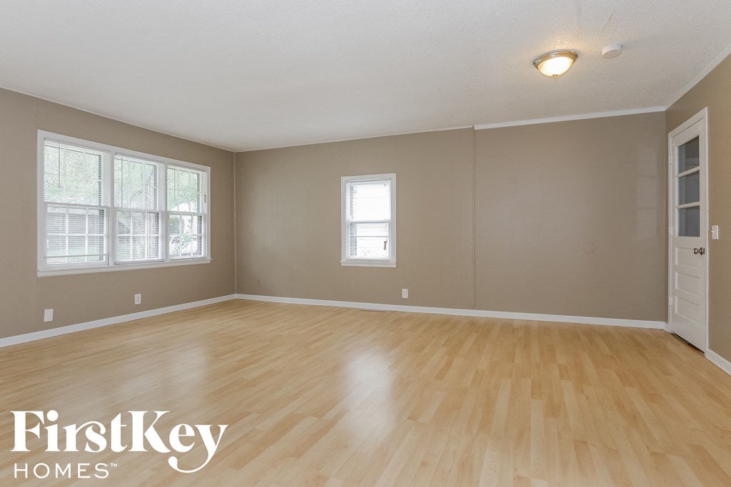 A room with wooden flooring and two windows.