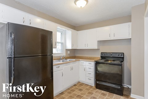 A kitchen with a black fridge and stove and white cabinets.