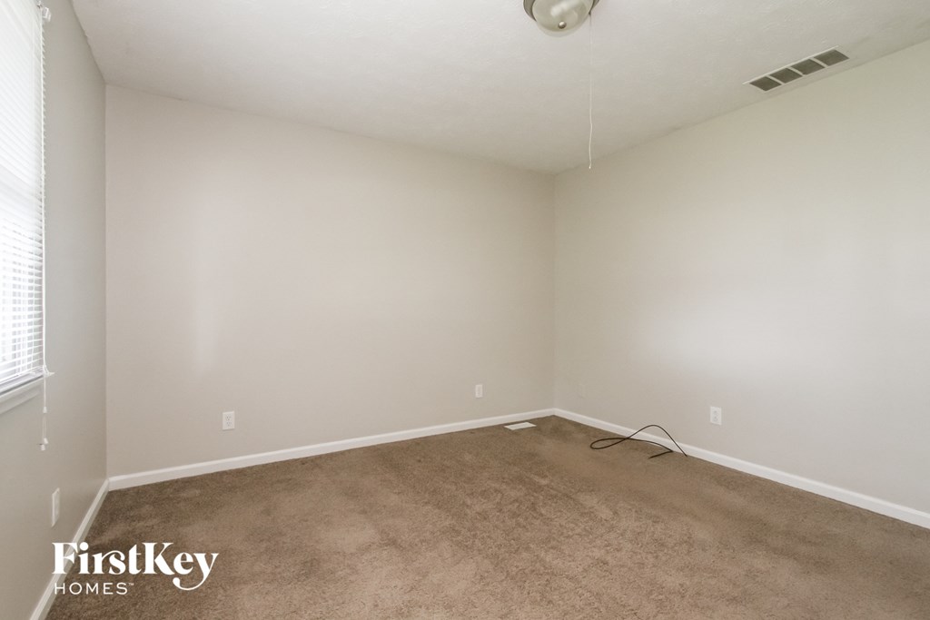 a carpeted room with a white wall and a ceiling fan