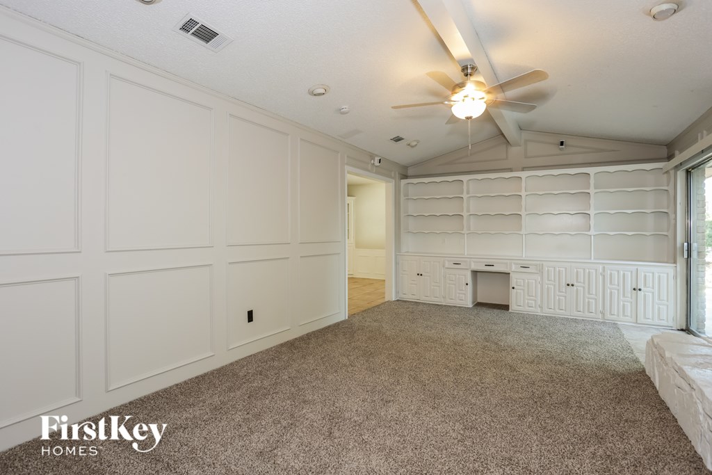 A spacious room with a carpeted floor, a ceiling fan, and a window with blinds.