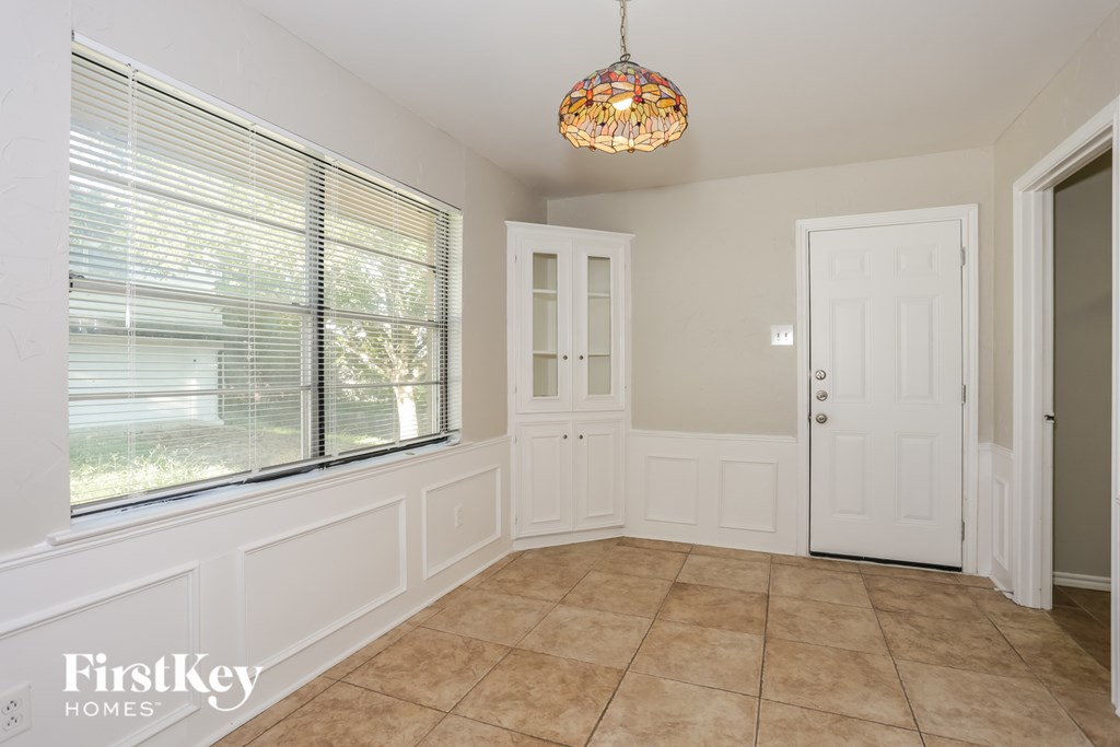 A room with a tiled floor, a window with blinds, a chandelier, and a door.