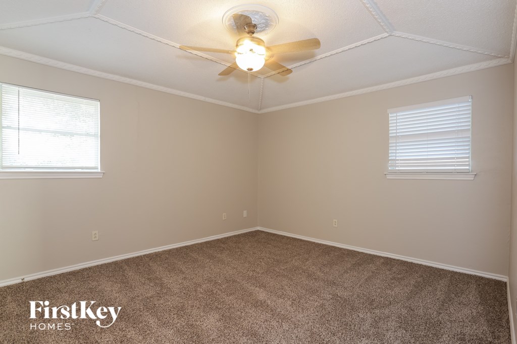 A room with a carpet floor, a ceiling fan, and two windows.