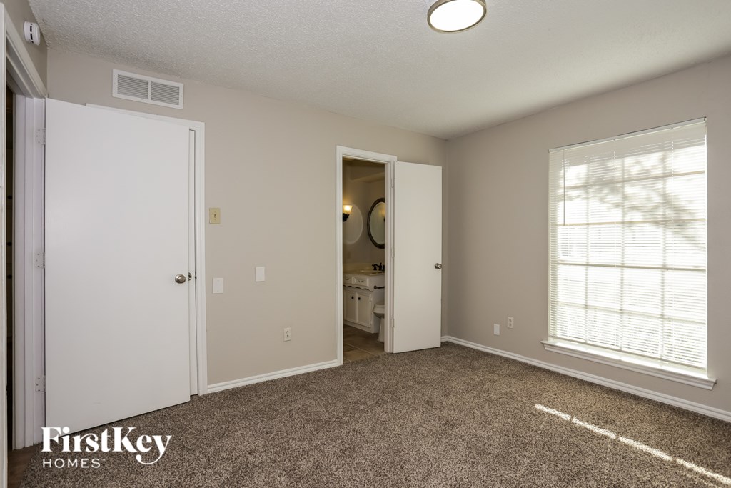 A bedroom with a carpeted floor and a window with blinds.