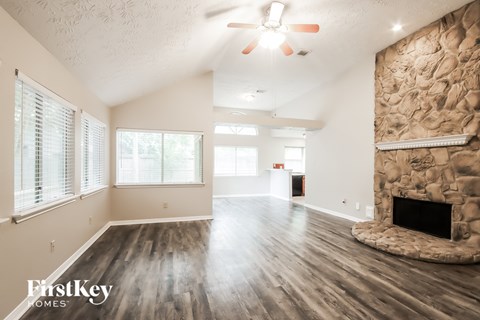 A spacious room with a stone fireplace and wooden floors.