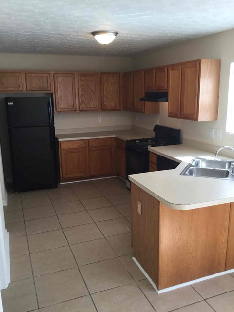 A kitchen with a black refrigerator and wooden cabinets.