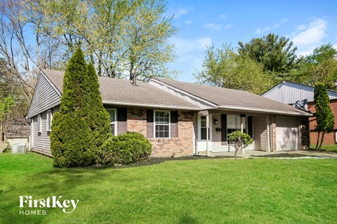 a white and brick house with a green lawn and trees