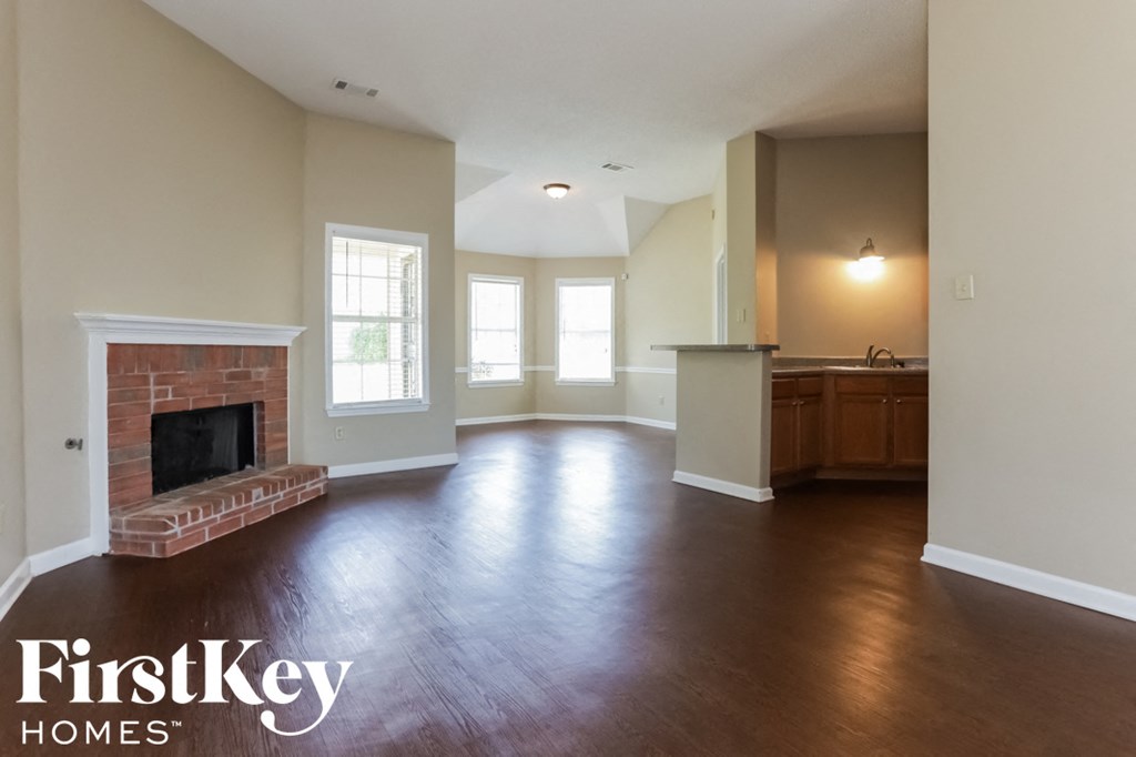 A spacious living room with a brick fireplace and wooden floors.