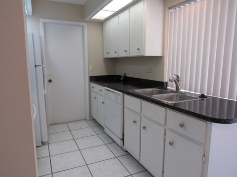 A kitchen with white cabinets and black countertops.