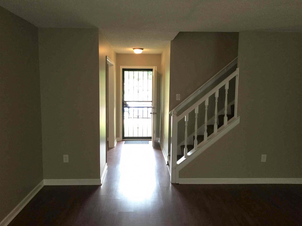 A hallway with a staircase leading to a door with a window.
