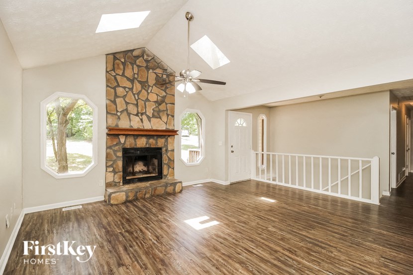 an empty living room with a stone fireplace and wooden floors