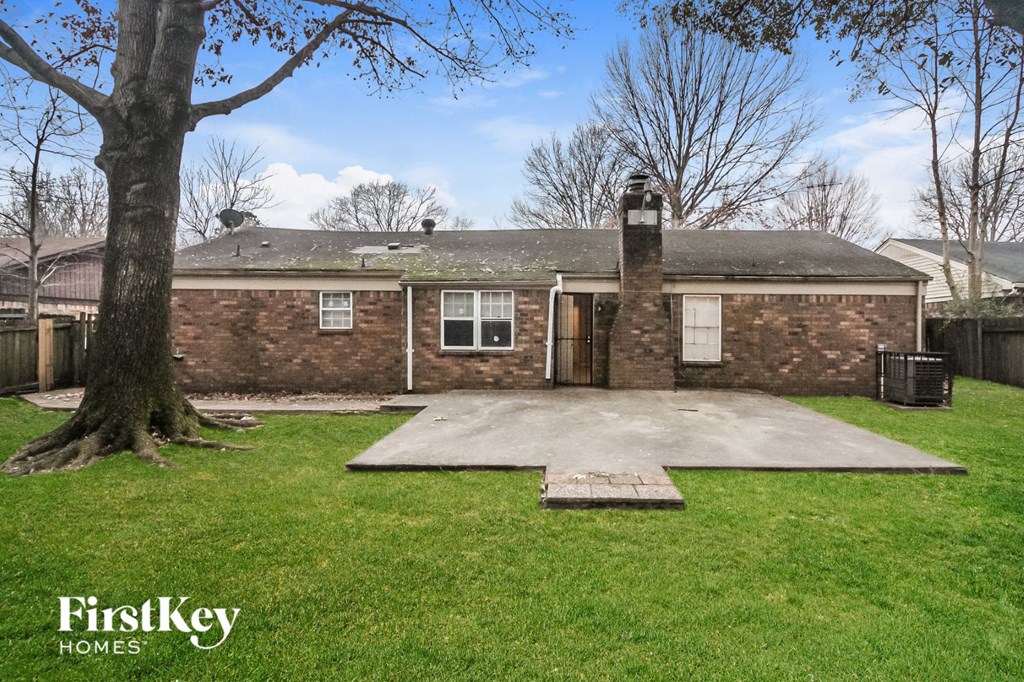the front of a brick house with a driveway and a tree
