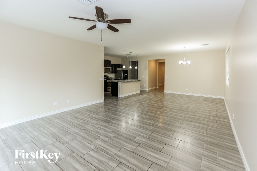 an empty living room with a ceiling fan and a kitchen