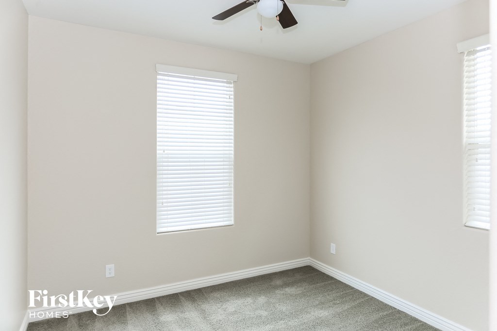 an empty room with two windows and a ceiling fan