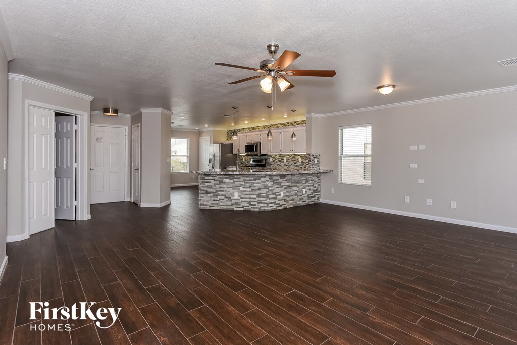 an empty living room with a ceiling fan and a kitchen