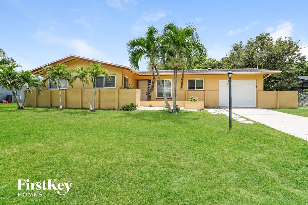 A yellow house with a white garage door and palm trees in front.