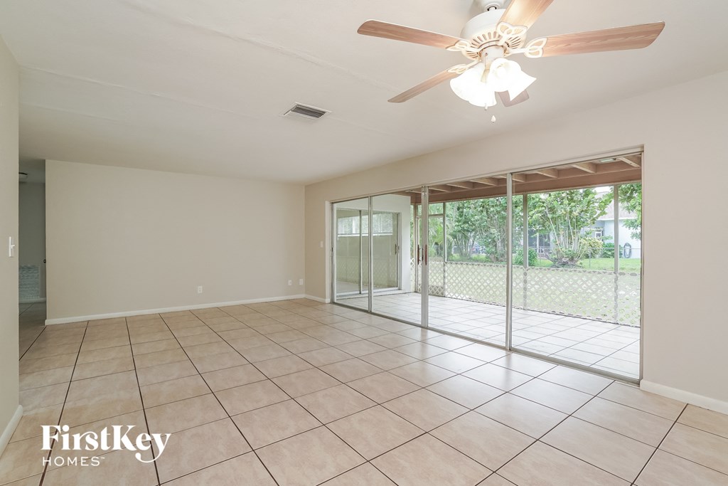A spacious room with a ceiling fan and sliding glass doors leading to a backyard.