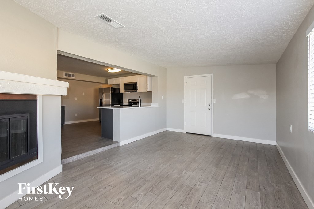 an empty living room with a fireplace and a kitchen