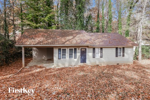 a small white house with a rusty roof in the woods