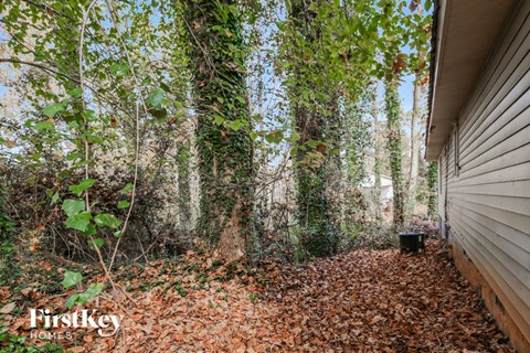 the side of a house in the woods with leaves and trees