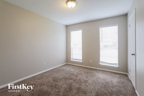a bedroom with carpet and two windows and a door