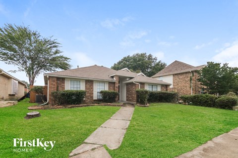 the front of a brick house with a lawn and a sidewalk