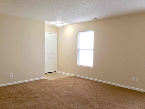 A room with a carpeted floor, a door, and a window.