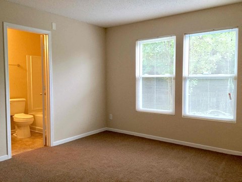 A room with a toilet and two windows.