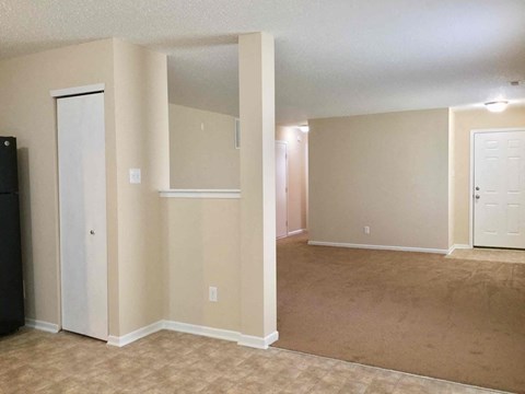 A room with beige walls and carpeting, a black refrigerator, and a white door.