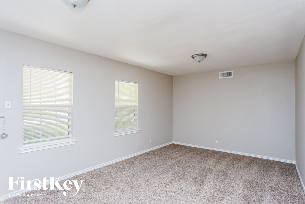 A room with a carpet floor and two windows.