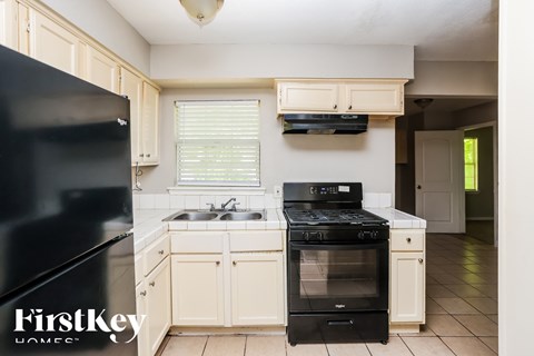 A black refrigerator is on the left of a kitchen with a black stove and oven.