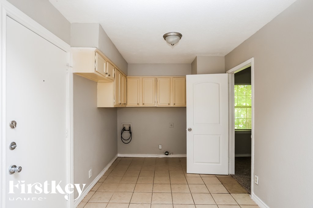 A white door opens to a small kitchen with beige cabinets.