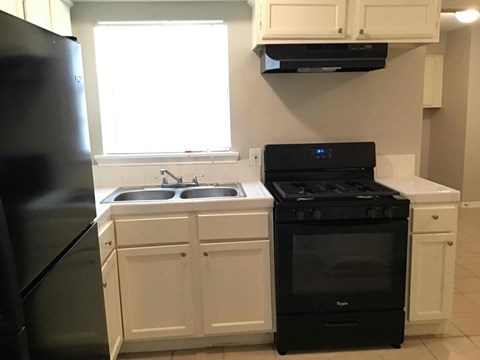 A black stove and sink in a kitchen with white cabinets.