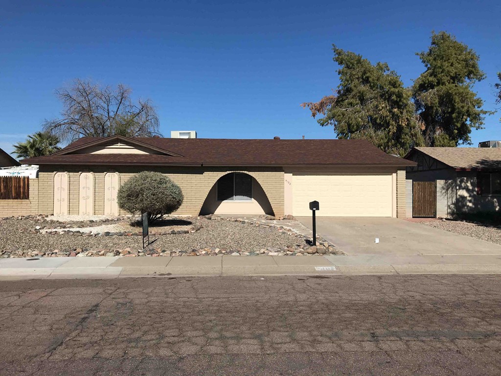 A house with a brown roof and a small tree in front.
