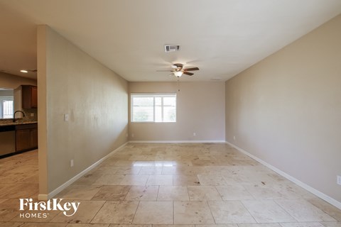 A spacious empty room with a ceiling fan and a window with blinds.