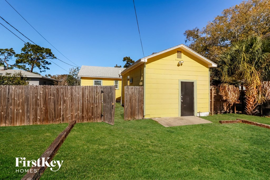 a small yellow house with a yard and a wooden fence