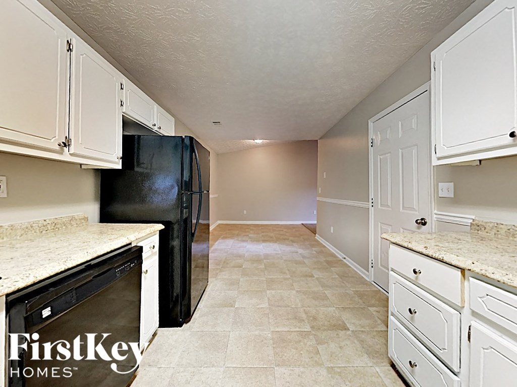 an empty kitchen with white cabinets and a black refrigerator