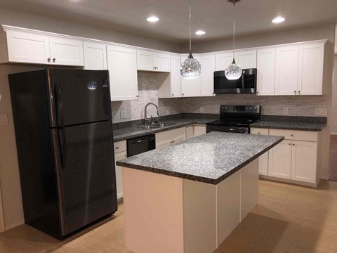 A black refrigerator is in a kitchen with white cabinets.